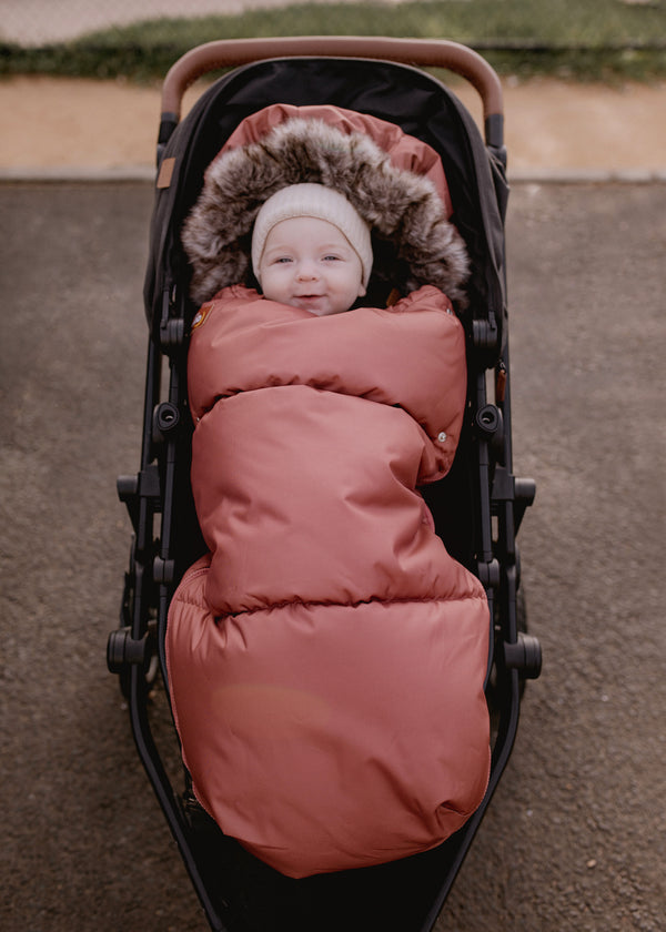 Baby boy in a stroller with a rust sleeping bag on a blurred outdoor background