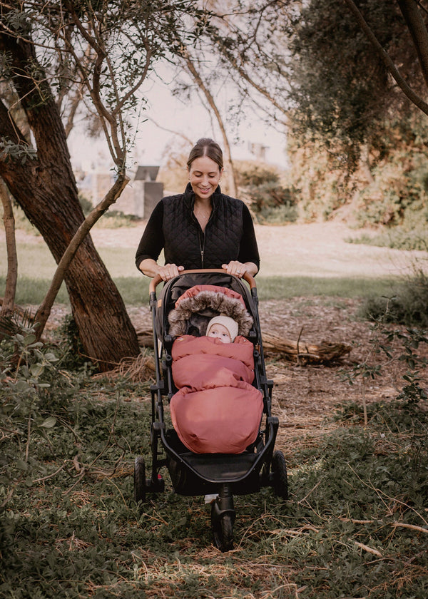 Woman pushing a stroller with a baby in a baby luno footmuff in a park forest setting