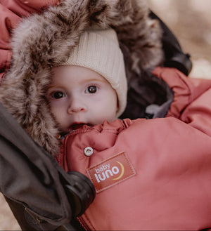 Baby in a baby luno footmuff with a fur hood peeking out from a stroller