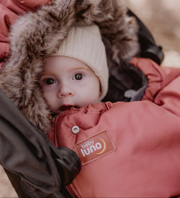 Baby in a baby luno footmuff with a fur hood peeking out from a stroller