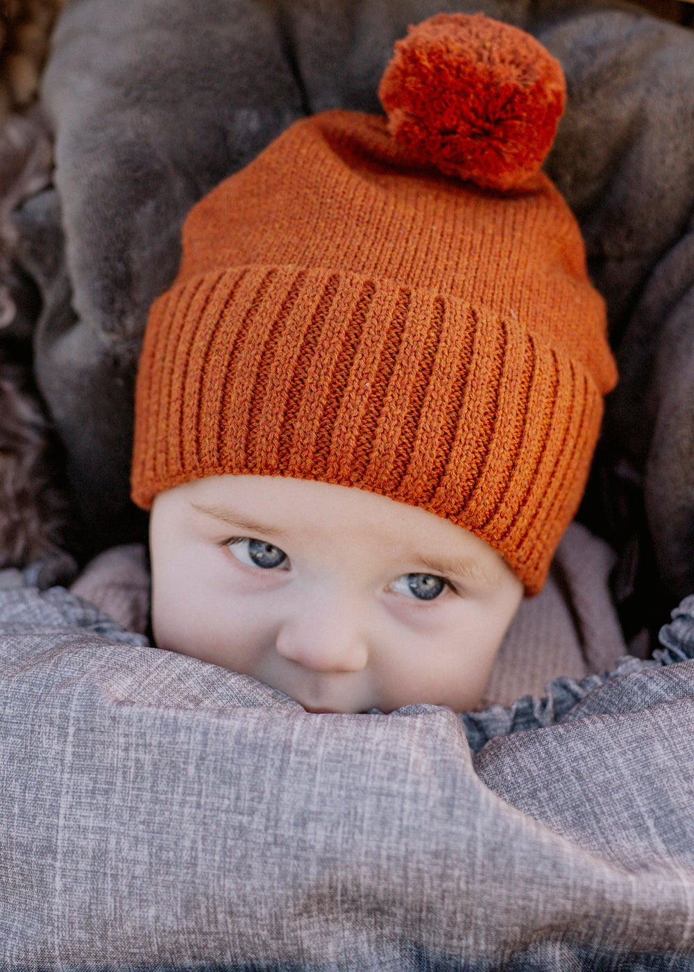 Brown knit beanie with a pom-pom on a white background