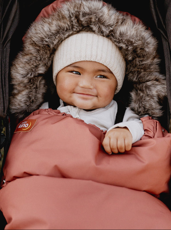 Child in a stroller with a fur-lined hood in the Terracotta baby luno Nordic Footmuff Pram Liner