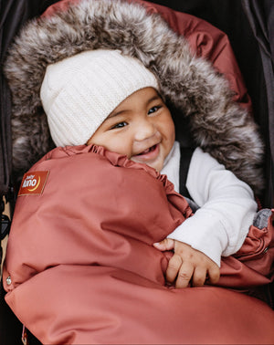 Child in a rust winter footmuff with fur hood in a stroller