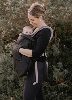 Woman carrying a baby in a carrier and with the baby luno Carrier Cocoon Winter Cover outdoors among trees