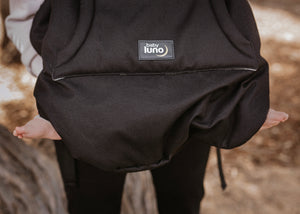 The baby luno Carrier Cocoon Winter Cover with baby feet sticking out on a blurred natural background
