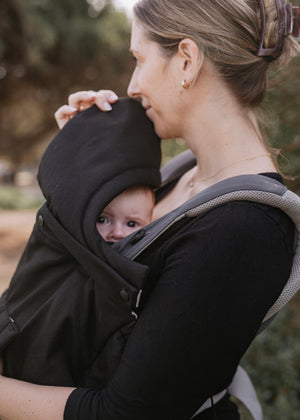 Woman carrying a baby in a black carrier with hood outdoors