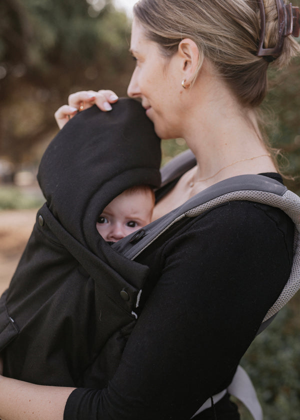 Woman carrying a baby in a black carrier with hood outdoors