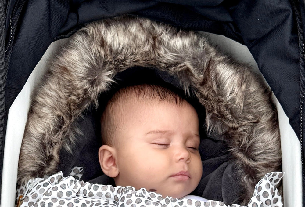 Baby sleeping in a stroller with a patterned swaddle blanket on a neutral background
